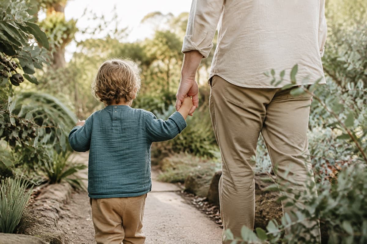 An adult and child walking hand in hand through a garden